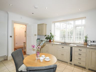 A kitchen with beige cabinets a round wooden table with two chairs and flowers in a vase at Awelfryn in Criccieth