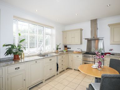 A kitchen with cream cabinets a stainless steel oven and extractor a round wooden table with flowers in a vase and chairs at Awelfryn in Criccieth