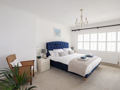 A bedroom with a blue bed frame two nightstands and a wicker chair at Awelfryn in Criccieth