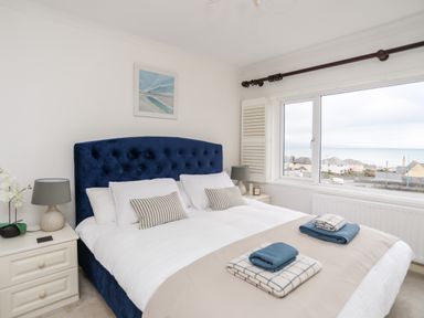 A bedroom with a blue upholstered bed and white bedding with folded towels on the bed at Awelfryn in Criccieth