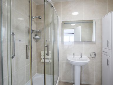 A bathroom with a glass shower enclosure a pedestal sink a wall mirror and a white cabinet at Awelfryn in Criccieth