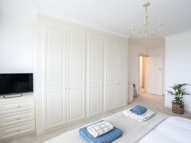 A bedroom with white wardrobes a television on a dresser and folded towels on a bed at Awelfryn in Criccieth