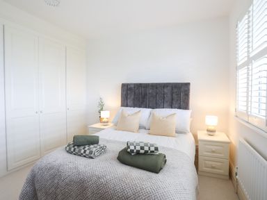 A bedroom with a bed with pillows bedside tables with lamps a wardrobe and a window with shutters at Awelfryn in Criccieth