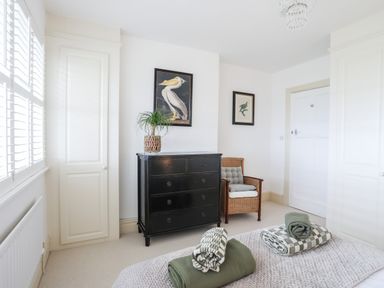 A bedroom with a black dresser a wicker chair and framed bird pictures on the wall at Awelfryn in Criccieth