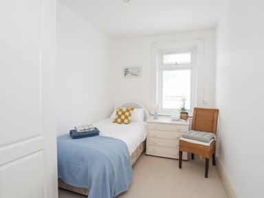 A small bedroom with a single bed a dresser a chair and a window at Awelfryn in Criccieth