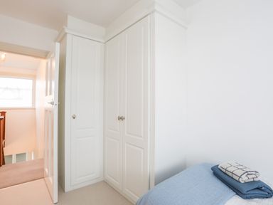 A bedroom corner with a white wardrobe an open door and a bed with folded blankets at Awelfryn in Criccieth