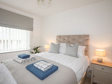 A bedroom with a bed side table lamp cushions and folded blankets at Awelfryn in Criccieth
