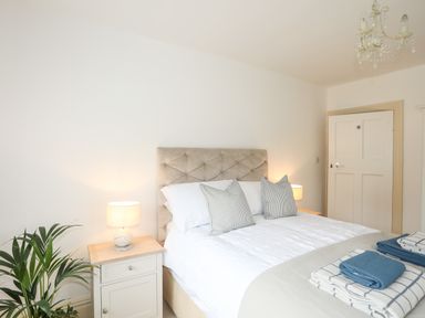 A bedroom with a bed bedside tables lamps a plant and folded towels at Awelfryn in Criccieth