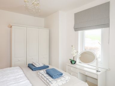 A bedroom with a bed a white wardrobe a dressing table with a mirror and window with blinds at Awelfryn in Criccieth