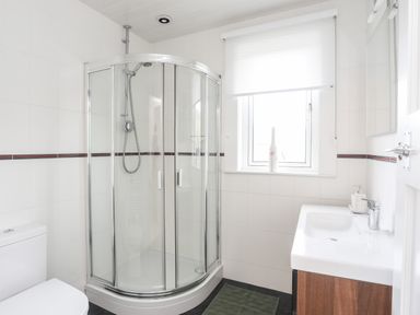 A bathroom with a corner shower, toilet, sink, and window at Awelfryn in Criccieth