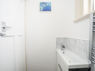 A small bathroom with a white door a rectangular sink with a faucet a marble backsplash and a painting of fish on the wall at Awelfryn in Criccieth