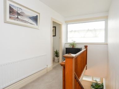 A hallway with wooden staircase railing a large window and a framed landscape picture on the wall at Awelfryn in Criccieth