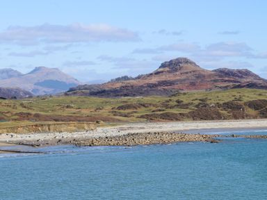 A rocky beach with water in the foreground and hills in the background at Awelfryn in Criccieth