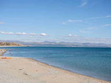 A sandy beach next to a calm sea with hills in the background at Awelfryn in Criccieth