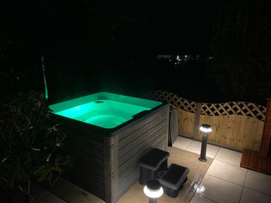 An illuminated outdoor hot tub with steps on a tiled patio at Awelfryn in Criccieth