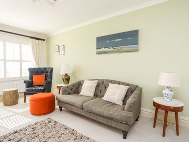 A living room with a sofa two side tables lamps an armchair and an orange ottoman at Awelfryn in Criccieth
