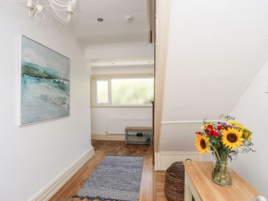 A hallway with a blue runner rug a bench under a window a wicker basket and a table with flowers at Awelfryn in Criccieth