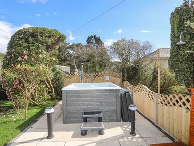 An outdoor hot tub with steps on a patio surrounded by a wooden fenced garden at Awelfryn in Criccieth