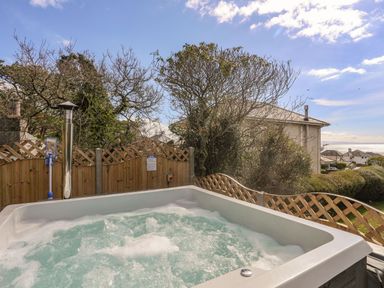 An outdoor hot tub with bubbling water surrounded by wooden fencing and trees near houses in Awelfryn Criccieth
