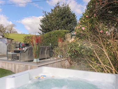 An outdoor hot tub with a patio area featuring wicker furniture and plants at Awelfryn in Criccieth