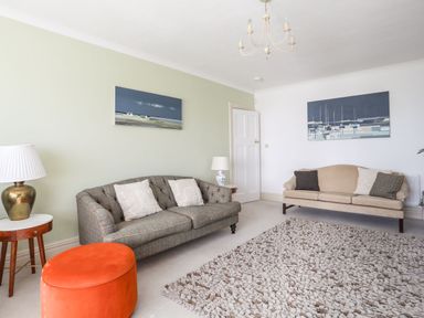 A living room with two sofas a round orange ottoman two side tables with lamps and two paintings on the walls at Awelfryn in Criccieth