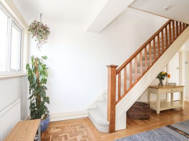 A staircase with wooden railing next to a console table with flowers and a basket underneath in a hallway at Awelfryn in Criccieth