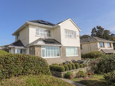 A two-story house with solar panels on the roof and a garden with trimmed bushes and outdoor furniture at Awelfryn in Criccieth