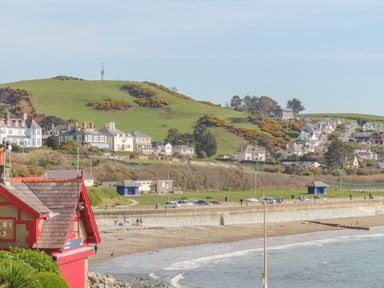 A beach with a seawall and houses on a hill behind at Awelfryn in Criccieth