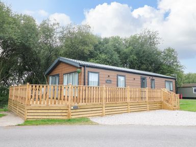 A wooden cabin with a raised deck and railing surrounded by trees at Barneys Retreat in Carnforth