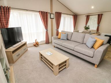 A living room with a gray sofa and cushions next to a wooden coffee table and a television on a wooden stand at Barney's Retreat in Carnforth