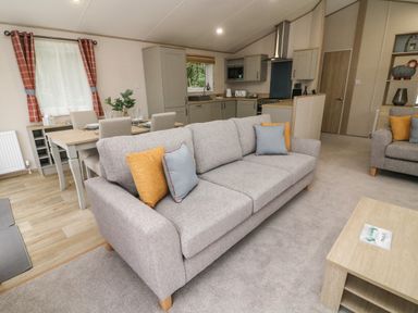 A living room with a gray sofa and cushions next to a wooden coffee table and dining table at Barney's Retreat in Carnforth