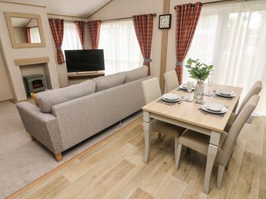A dining area with a table set for four and a living room with a sofa and television at Barneys Retreat in Carnforth