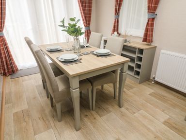 A dining area with a wooden table set for four with beige chairs and red plaid curtains at Barneys Retreat in Carnforth