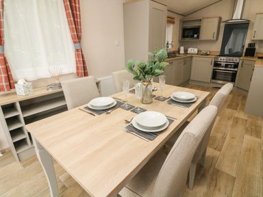 A dining table set with plates glasses and cutlery in a kitchen with cabinets and appliances at Barneys Retreat in Carnforth