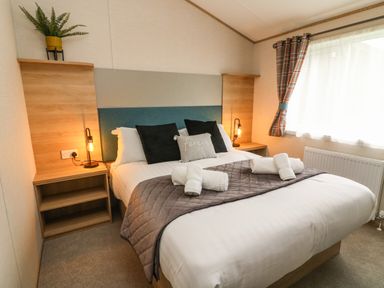 A bedroom with a double bed two shelves bedside tables lamps a plant and a window with plaid curtains at Barneys Retreat in Carnforth