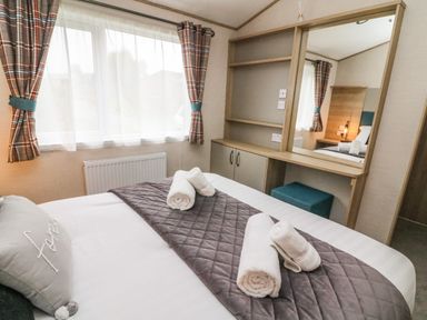 A bedroom with a bed with rolled towels on a blanket and a vanity with a mirror and stool at Barneys Retreat in Carnforth