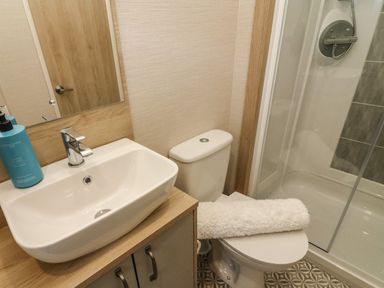 A bathroom with a sink, toilet with a white towel on it, and a shower enclosure at Barneys Retreat in Carnforth