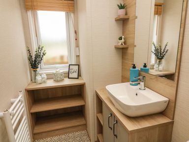 A bathroom with a sink vanity unit mirror a window with a blind and wooden shelves with plants at Barneys Retreat in Carnforth
