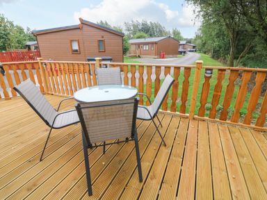 A wooden deck with a glass round table and four chairs outside wooden cabins at Barneys Retreat in Carnforth