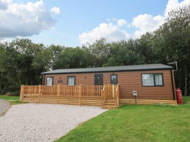 A brown single-story cabin with a wooden fence and steps in front with trees behind at Barneys Retreat in Carnforth