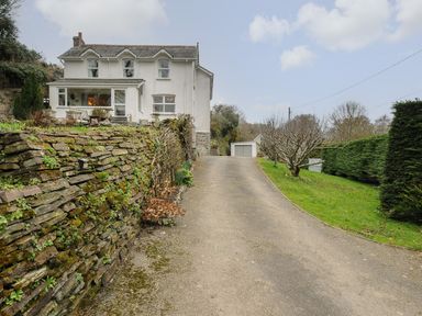A driveway leading to a white house with a stone retaining wall and garage at Kirland in St Kew Highway