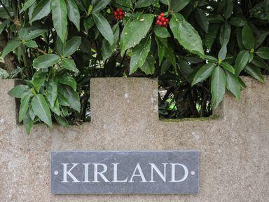 A stone wall with a slate plaque reading Kirland green leaves and red berries behind the wall