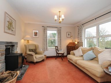 A living room with an armchair sofa wooden chair wooden cabinet and a fireplace at Kirland in St Kew Highway