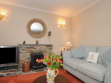 A living room with a stone fireplace a round mirror a television a vase with flowers and a sofa with cushions at Kirland in St Kew Highway