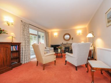A living room with upholstered armchairs a wooden cabinet floral curtains and a fireplace at Kirland in St Kew Highway