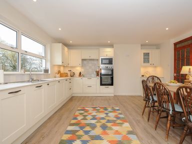 A kitchen with white cabinets a dining table with wooden chairs and a colorful rug on wooden floor at Kirland in St Kew Highway