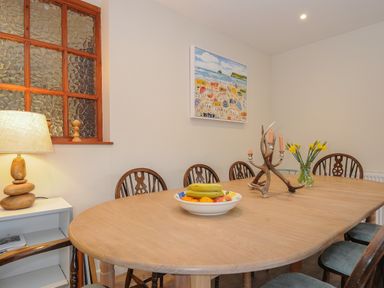 A dining room with a wooden table and chairs a bowl of fruit a vase of flowers a candle holder a lamp and a painting on the wall at Kirland in St Kew Highway