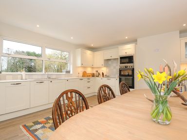 A kitchen with white cabinets wooden dining table with wooden chairs and yellow flowers in a vase at Kirland in St Kew Highway