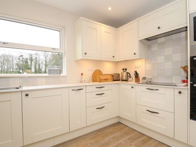 A kitchen with white cabinets a microwave toaster kettle and cutting board at Kirland in St Kew Highway