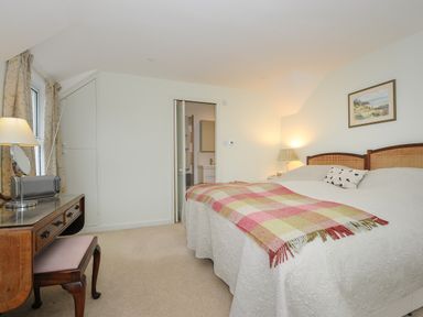 A bedroom with a double bed covered with a blanket and a plaid throw a wooden dressing table with a lamp and mirror at Kirland in St Kew Highway